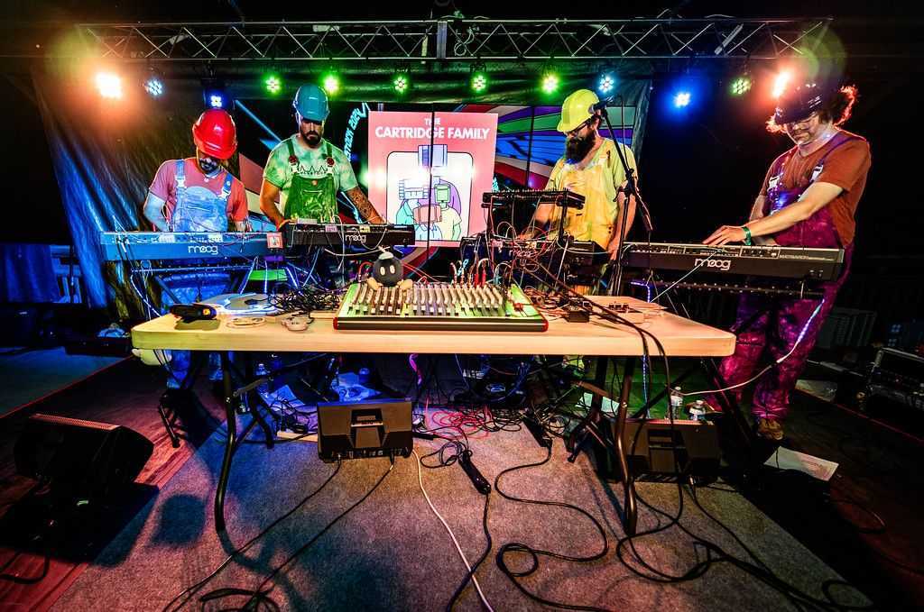 An image of the four members of The Cartridge Family standing at their synths, performing at MAGStock.