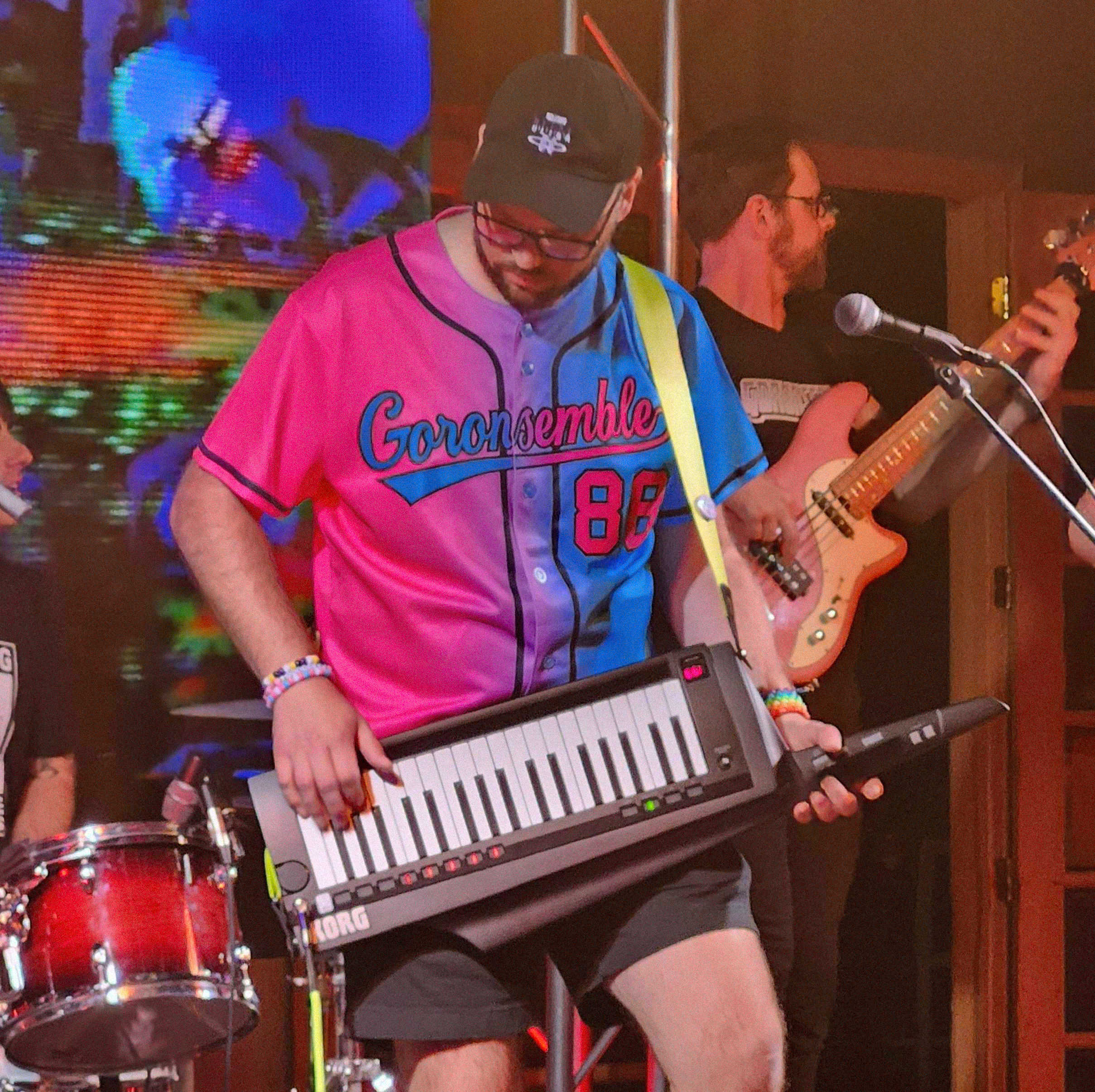 An image of performer Biggoron. He is engaged in a show holding a keytar while wearing a signature Biggoron baseball jersey and the Goronsemble band plays in the background.