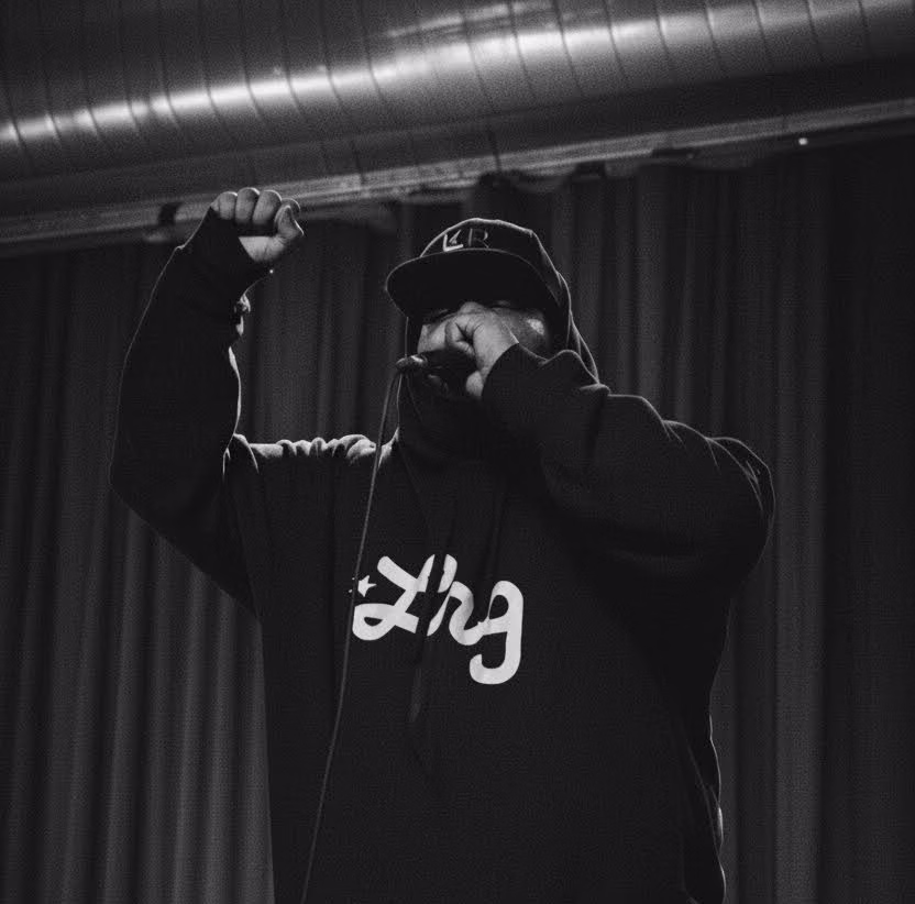 A photo of MAGStock Performer Ardamus is displayed. A constrasting greyscale photo shows Ardamus amidst a passionate performance. His microphone is in hand and raised to his mouth, while his other hand is in the air with fingers curled powerfully into a fist.