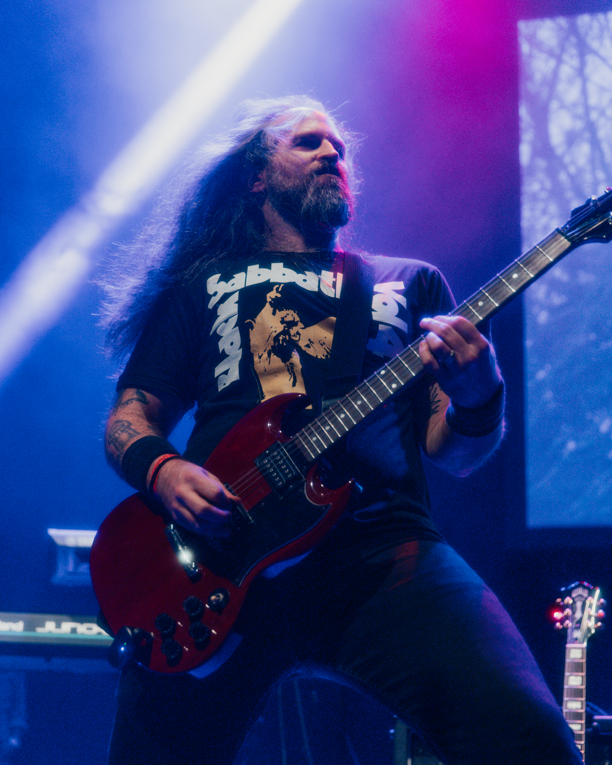 An image of MAGStock performer Mega Beardo is displayed. Ryan leans back powerfully with guitar in-hand; hair blowing back while actively engaged in a stage performance.